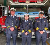 Three uniformed men stand beside a fire truck